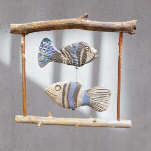 Zwei handgefertigte Keramikfische in Blau- und Erdtönen, hängend an einem Holzrahmen, ideal für maritime Fensterdekoration.