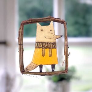 Keramisches Deko-Mobile mit einem Fuchs in gelber Kleidung, umgeben von einem Holzrahmen, ideal für Fensterdekoration.