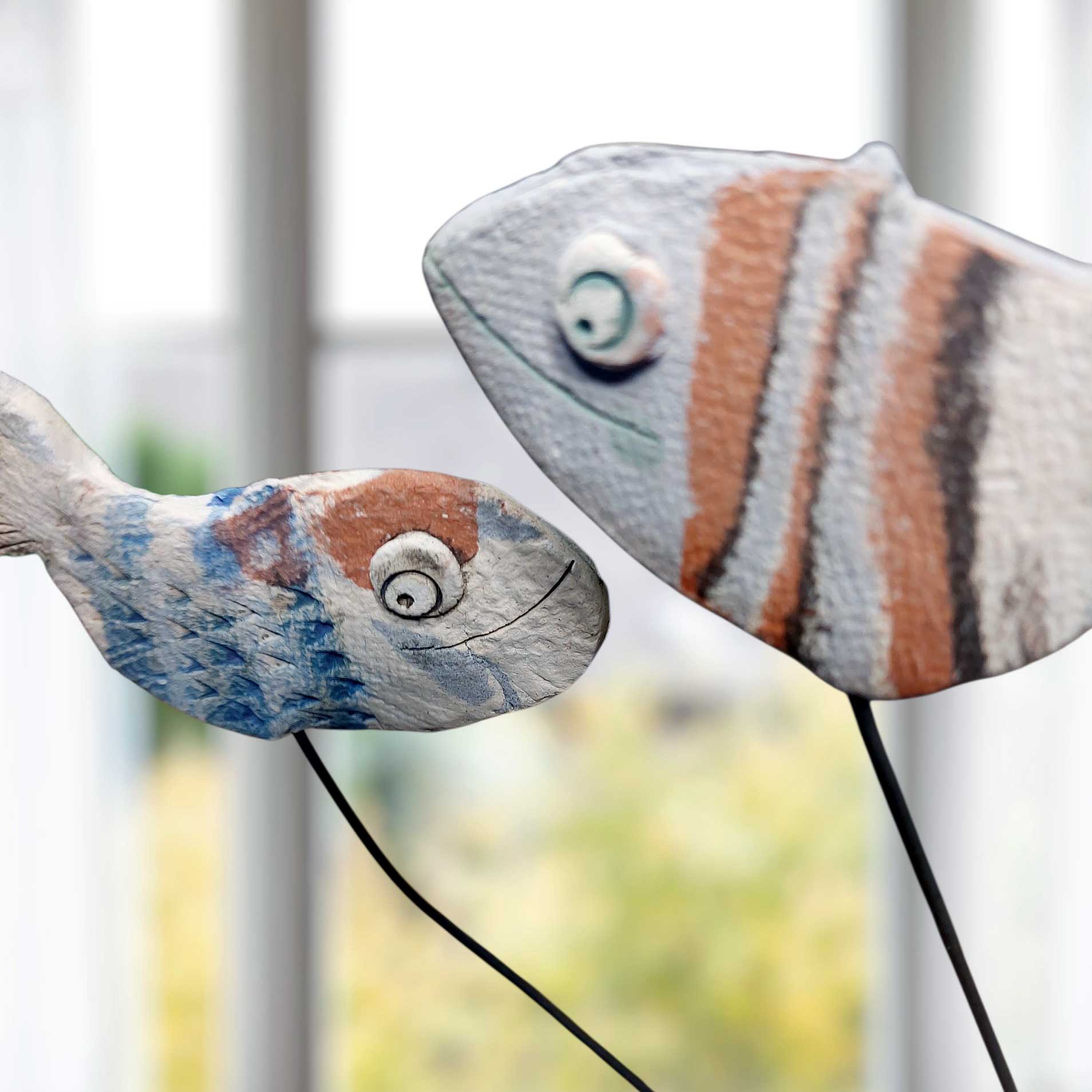 Zwei handgefertigte Keramikfische in Blau und Braun auf Metallstäben als maritime Gartendeko oder dekorativer Aufsteller für ein maritimes Ambiente.