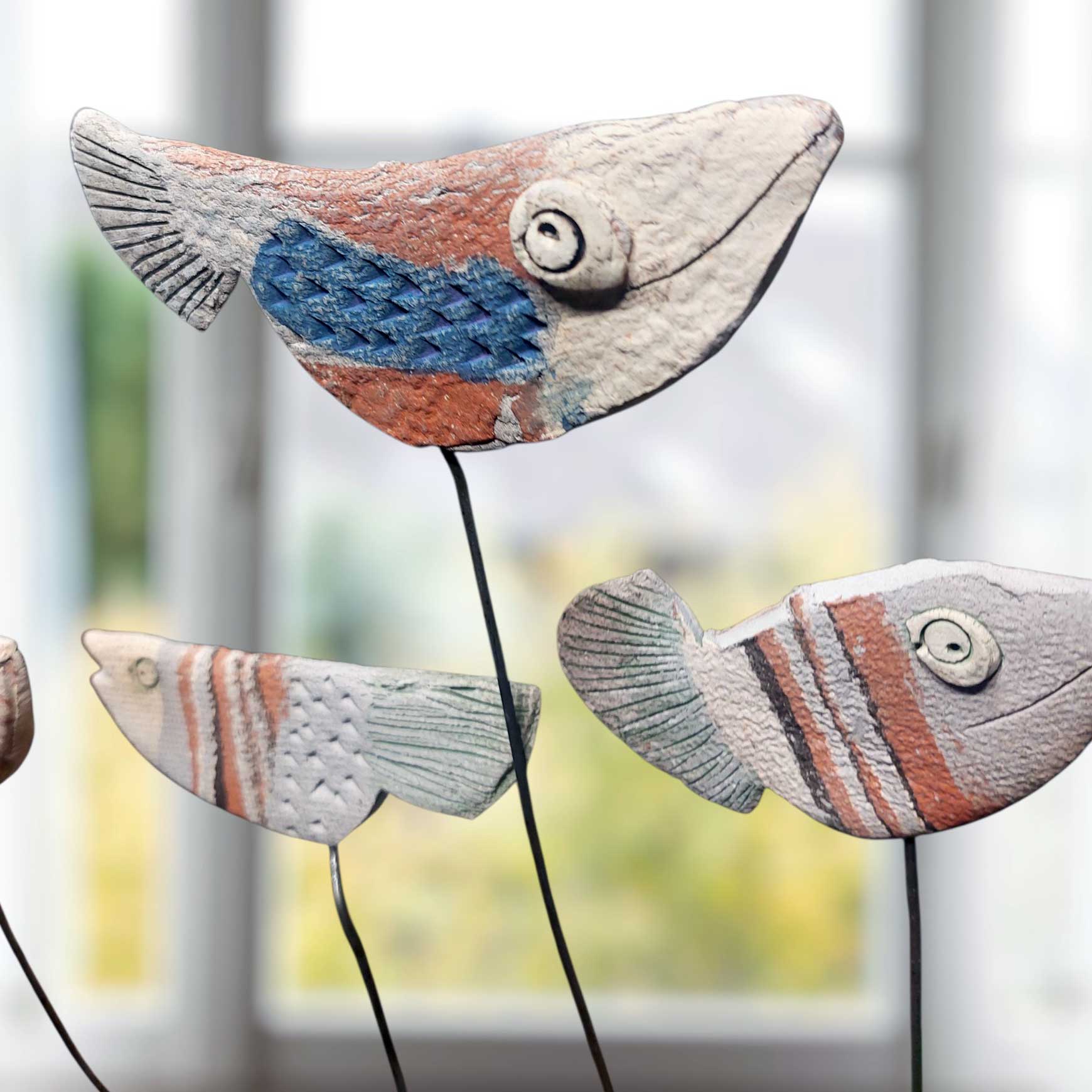 Handgefertigter Maritimer Keramik-Fischschwarm auf Metallstäben als dekorative Gartenstecker mit strukturierter Oberfläche in Blau und Erdtönen.