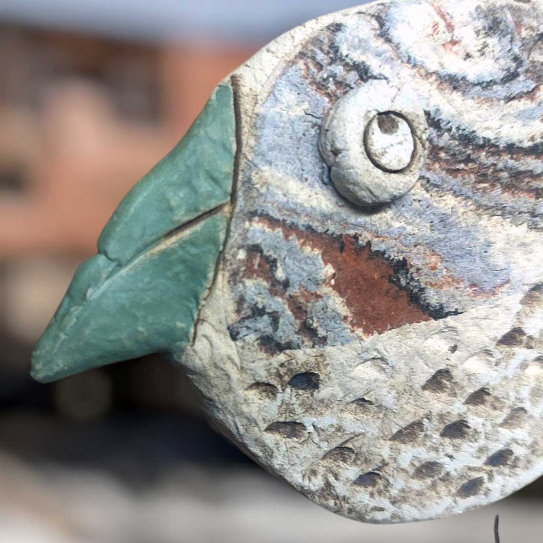 Nahaufnahme vom Kopf des Sturmvogel Keramik Vogel mit grünem Schnabel und strukturierter, handbemalter Oberfläche als dekorative Fensterdeko.