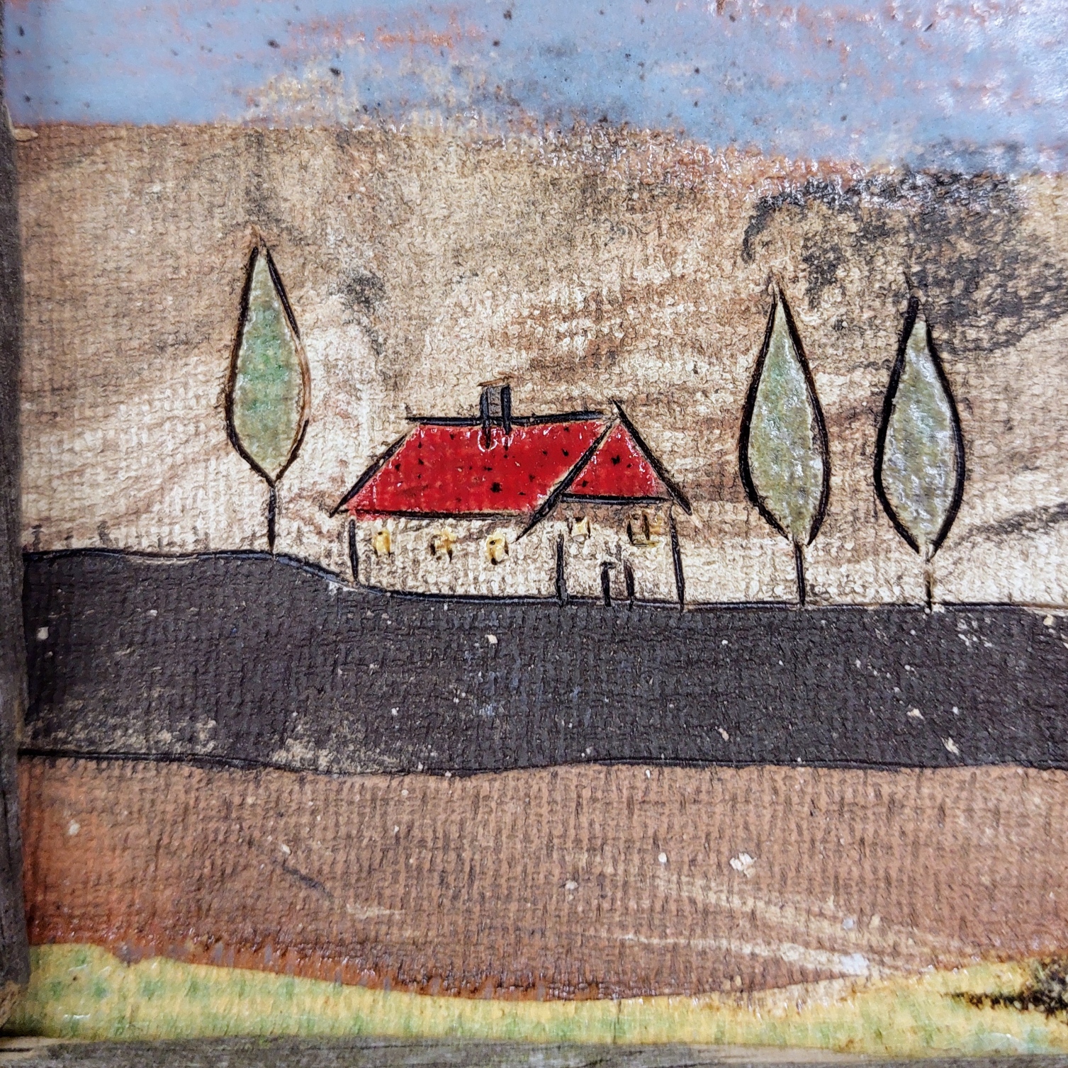 Handgearbeitete Keramikfliese mit naiver Landschaft, rotem Haus und Bäumen in einem rustikalen Rahmen aus Altholz als dekoratives Wandbild für Zuhause.