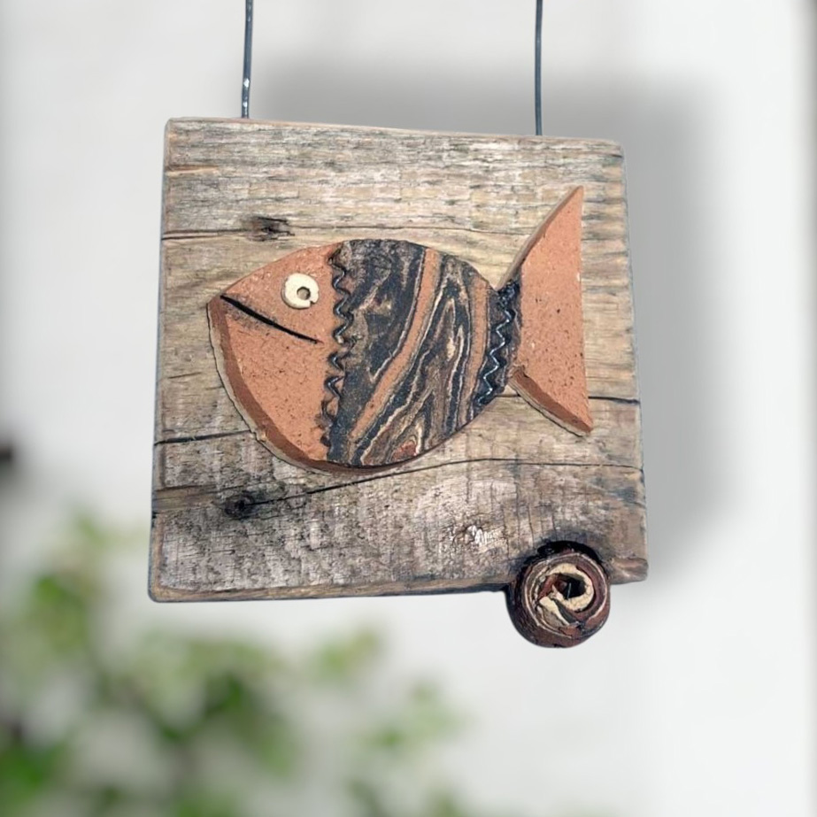 Hängende Wanddekoration aus Keramik in Fischform auf einem rustikalen Stück Altholz, ideal als maritime Dekoration für Haus und Garten.